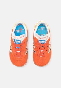 Oranžové semišové tenisky s černými skvrnitými detaily, bílými tkaničkami a modrým vnitřkem s motivem Pixar. Na jazyku je značka Adidas.