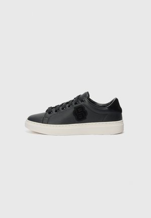 Sneakers neri sintetici a basso profilo con una superficie liscia, suola bianca e logo nero laterale. Presentano lacci neri e un design minimalista.