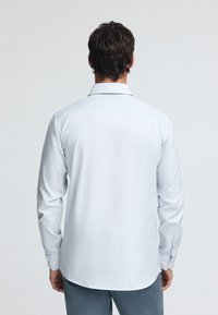 Camicia bianca a maniche lunghe con un motivo a scacchi azzurro chiaro, con polsini a bottone e colletto classico, realizzata in un tessuto morbido.