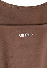 Hnědá látka se hladkým povrchem, s bílým logem "aimn" poblíž výstřihu, zdůrazňující jednoduchý design a moderní vzhled.