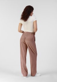 Pantalons larges à rayures en tissu rose, présentant une coupe décontractée, une taille élastique et des rayures blanches verticales. Associés à un haut beige ajusté.