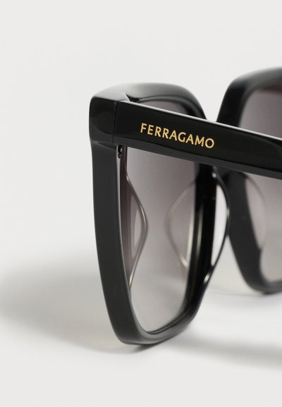 Lunettes de soleil rectangulaires noires oversize avec verres teintés dégradés et logo "Ferragamo" doré sur la branche.