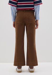 Pantalones de pana marrones con un diseño de pierna acampanada, que cuentan con dos bolsillos traseros. Combinados con una camiseta de rayas y zapatillas. Textura suave.