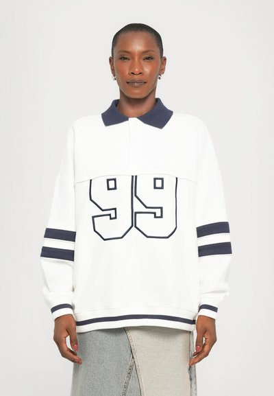 Sudadera blanca de polo con cuello y puños en azul marino, presenta un gran "99" en la parte frontal y rayas horizontales en azul marino en las mangas.