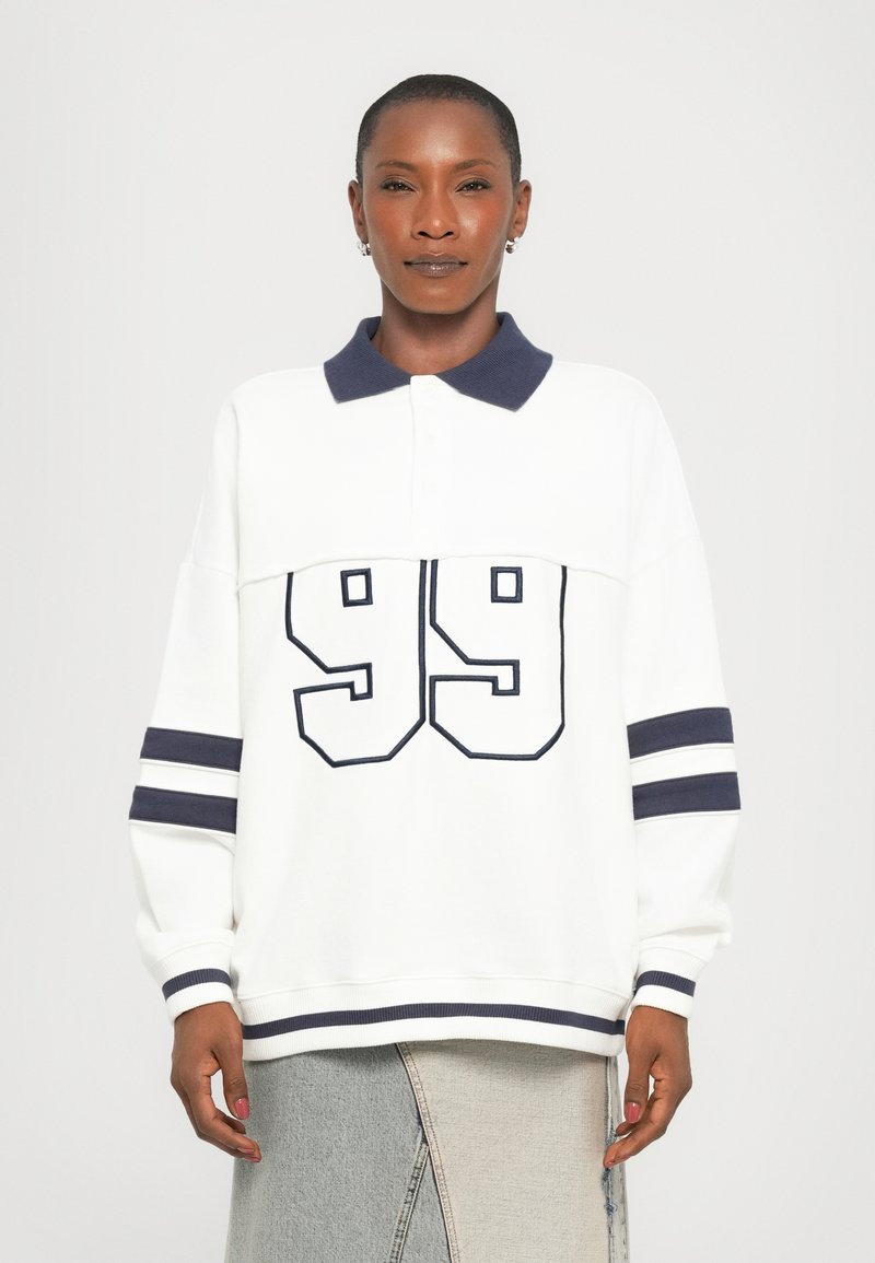 White polo sweatshirt with navy collar and cuffs, features a large navy "99" on the front and horizontal navy stripes on the sleeves.