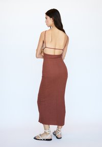 Rustinvärinen, tiukan maxi-mekko, jossa on spagettiolkaimet, teksturoitu kangas ja avoin selkädesign. Yhdistetty litteiden, nauhakiinnitteisten sandaalien kanssa.