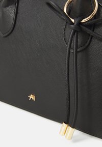 Borsa nera con texture, caratterizzata da hardware in tonalità dorata, doppie coulisse e un sottile accento con logo sulla parte anteriore. Finitura liscia.