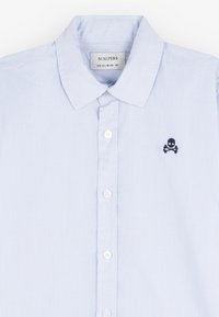 Camicia a righe azzurro chiaro con colletto classico e ricamo di teschio e ossa incrociate in nero. Include bottoni bianchi lungo la parte anteriore.