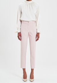 Pantalons ajustés rose clair avec une coupe slim, dotés d'une fermeture à bouton doré et de coutures latérales discrètes, associés à un blouse en soie crème.