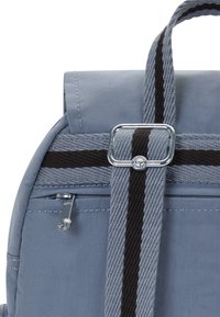 Ljusblå tygryggsäck med svartrandig justerbar rem, silverfärgad spänne och en liten ficka med dragkedja på baksidan.