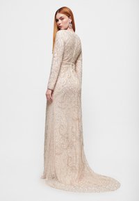 Perlenbesetztes Langarmkleid in zartem Blush mit kunstvollen Wirbelmustern, einem taillierten Oberteil und einem fließenden Zug. Detaillierter Rücken mit Reißverschluss.