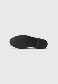 Semelle de chaussure noire avec un motif de grip texturé, légèrement arrondie, et logo Gabor en relief. Présente une finition lisse et durable.