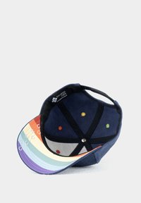 Navy baseball cap with a rainbow-striped brim. Interior features colorful eyelets and a branded label. Soft fabric, structured shape.