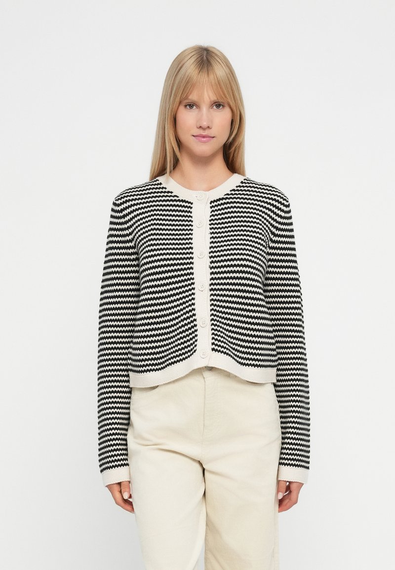 Cardigan a righe bianche e nere con design corto, scollatura rotonda e chiusura con bottoni frontali. Realizzato in materiale lavorato a maglia.