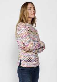 Pull en tricot multicolore avec un design aéré et lâche, sur des teintes de rose, jaune et vert. Fentes sur les côtés à l'ourlet.