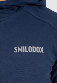 Sudadera azul marino hecha de tela suave, con capucha y texto gris "SMILODOX" en el frente. Textura lisa con costuras reforzadas.