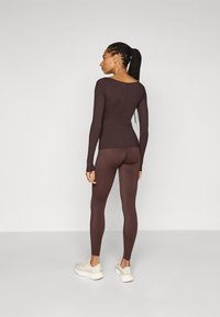 Langärmliges, enganliegendes Oberteil und passende Leggings in Dunkelbraun, aus dehnbarem Material. Mit Rundhalsausschnitt und nahtlosem Design ausgestattet.