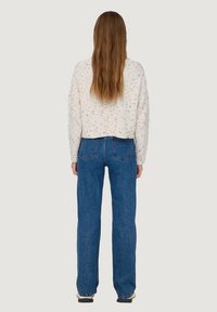 Cropped white sweater with multicolored specks, paired with high-waisted blue jeans featuring a straight leg and back pockets.