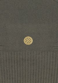 Dunkelgrüner Strickbeanie mit gerippter Textur, ausgestattet mit einem dekorativen goldenen runden Emblem mit einem filigranen Blumendesign.