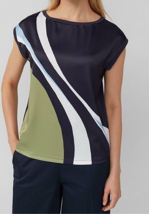 Vrouw draagt een mouwloze marineblauwe top met abstracte gebogen strepen in wit, blauw en olijfgroen, gecombineerd met donkerblauwe broek.