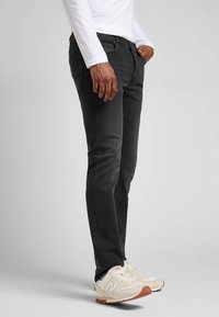 Svarta denimjeans med slim fit, framfickor och subtila sömdetaljer, parat med gräddfärgade sneakers med röda accenter.