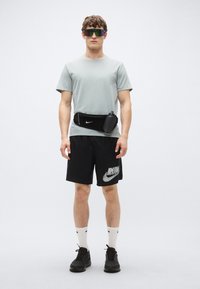 Grå kortärmad t-shirt, svarta shorts med "RUN"-tryck, svart midjeväska, vita strumpor med svarta detaljer, mörka sneakers och reflektiva solglasögon.
