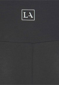 Leggings de sport noirs avec une texture côtelée, une taille haute et un logo "LA" blanc dans un carré au centre.