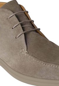 Zapato de ante marrón claro, de altura hasta el tobillo, con puntera mocasinera cosida, tres ojetes con cordones finos y una suela de goma lisa.