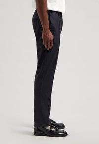 Granatowe, dopasowane spodnie cywilne o gładkiej fakturze, z bocznymi kieszeniami i płaskim przodem, zestawione z błyszczącymi czarnymi mokasynami.