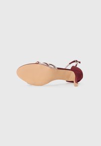 Burgundy korkokengät, joissa on satiinipinta, ohuet korot, teksturoitu beige pohja ja metalliset nauhat edessä.