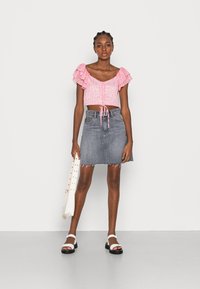 Top curto rosa com mangas de babados e laço na frente, combinado com uma saia mini de ganga cinza com bainha desfiada e sandálias brancas de plataforma.