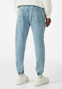 Světlé modré džíny s elastickým pasem a zúženými kotníky. Mají dvě zadní kapsy, standardní švy a měkký, texturovaný povrch.