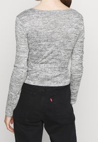 Maglietta grigia a maniche lunghe con texture a puntini, caratterizzata da una vita aderente e un collo a giro, abbinata a pantaloni neri a vita alta con due tasche posteriori.