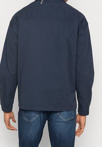 Marinblå, lätt jacka med avslappnad passform, långa ärmar och elastiska muddar. Har en klassisk krage och en smidig textur.