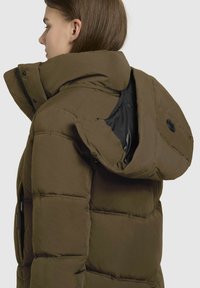 Brauner Pufferjacke mit abnehmbarer Kapuze. Sie verfügt über einen Reißverschluss, strukturierte Stoff und ein schwarzes Innenfutter.
