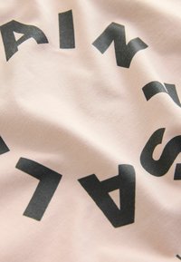Šviesiai rožinė medžiaga su ryškiu juodu tekstu, šiek tiek tekstūriniu paviršiumi, demonstruojanti išbarstytas raides apskritoje formacijoje.