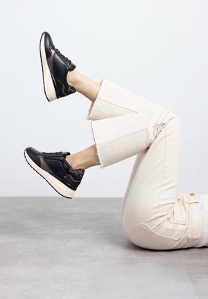 Zapatillas de cuero negro con acentos texturizados, suela crema y puntera reforzada; combinadas con pantalones cortos de color beige claro con dobladillo deshilachado.