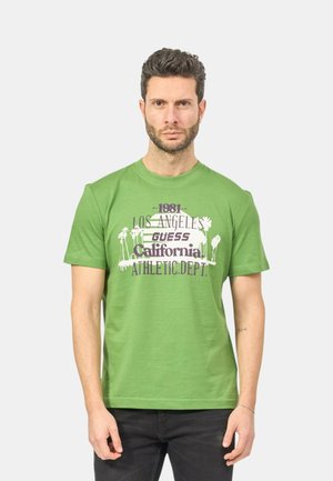 Maglietta in cotone verde con un design grafico bianco e viola che presenta palme e la scritta "Los Angeles Guess California Athletic Dept."