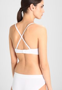 Reggiseno bianco con spalline incrociate, chiusura posteriore regolabile e texture liscia; abbinato a slip bianchi coordinati.