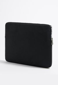 Funda para portátil negra hecha de material texturizado, con cierre de cremallera y detalle del logo en un lateral. Forma rectangular con esquinas redondeadas.