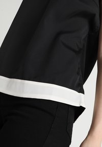 Top nero con orlo bianco, in tessuto liscio e design rilassato. Il tessuto ha una leggera lucentezza, che esalta il suo aspetto moderno.