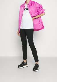 Snygg rosa overshirt, vit t-shirt med svart text, svarta åtsittande byxor och svarta träningsskor med guldaccent.