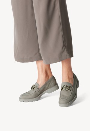 Svetlo sive usnjene loafer čevlji z debelo verižico, nošeni z taupe širokimi skrajšanimi hlačami na bosih nogah.