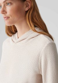 Maglione beige chiaro con cappuccio realizzato in tessuto a maglia testurizzata, dotato di un collo rilassato e materiale morbido e traspirante per il massimo comfort.
