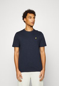 T-shirt in cotone blu navy con maniche corte, caratterizzato da un piccolo emblema giallo a forma di aquila sul lato sinistro del petto; texture liscia, design classico con scollo a girocollo.