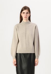 Beige stickad tröja med hög halsringning, ribbade ärmslut och rak passform. Parat med en kjol i svart läder. Strukturerad finish.