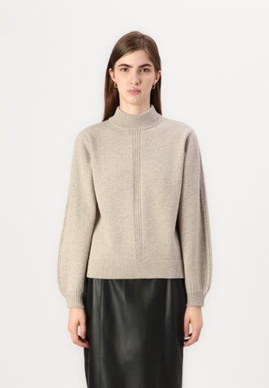 Beige knitted sweater with a high neckline, ribbed cuffs, and a straight fit. Paired with a black leather skirt. Textured finish.