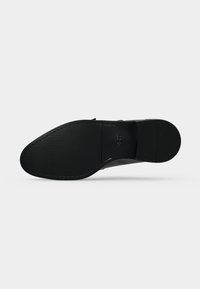 Semelle d'une chaussure de ville noire avec une texture lisse, des coutures le long des bords et le nom de la marque embossé près du talon.