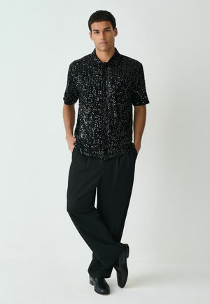 Black short-sleeve shirt with sequins, slim fit, paired with black wide-leg trousers and shiny black shoes. Light background.