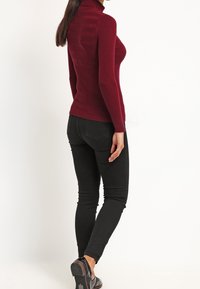 Maglione a collo alto bordeaux con strisce testurizzate, design aderente. Abbinato a jeans skinny neri e scarpe nere eleganti. Stile minimalista.